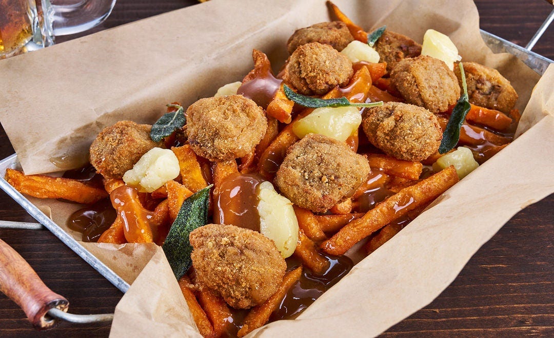A paper-lined tray with sweet potato fries, breaded beef bites and cheese curds with gravy