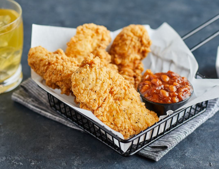 Basket of fully cooked homestyle pepper chicken tenderloin fritters with crispy breading, served with baked beans and a drink on the side