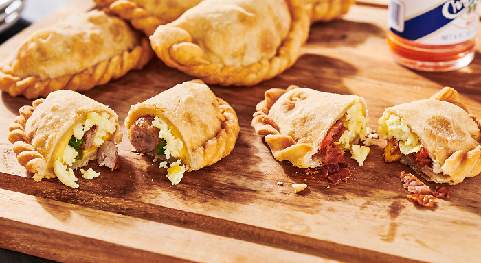 A wooden plate featuring two breakfast empanadas with sausage and eggs inside