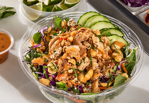a salad of greens, slices of cucumber, quinoa and vegetables, topped with chicken