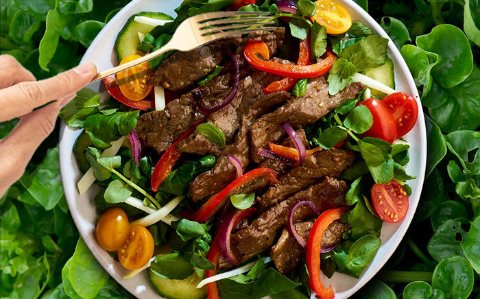 greens topped with sliced steak, red bell pepper slices, sliced cucumber, sliced red onion and sliced red and yellow cherry tomatoes