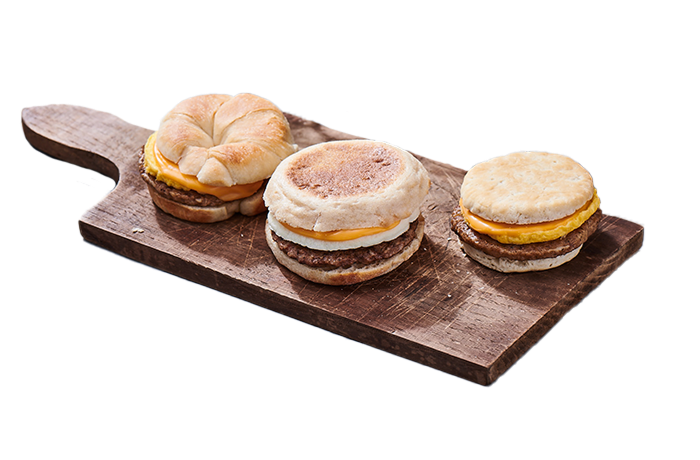 A wooden serving board holding three breakfast sandwiches