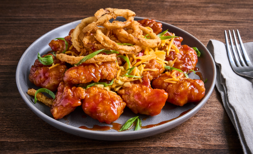 A plate piled high with boneless wings covered in a whiskey barbecue and onion rings.