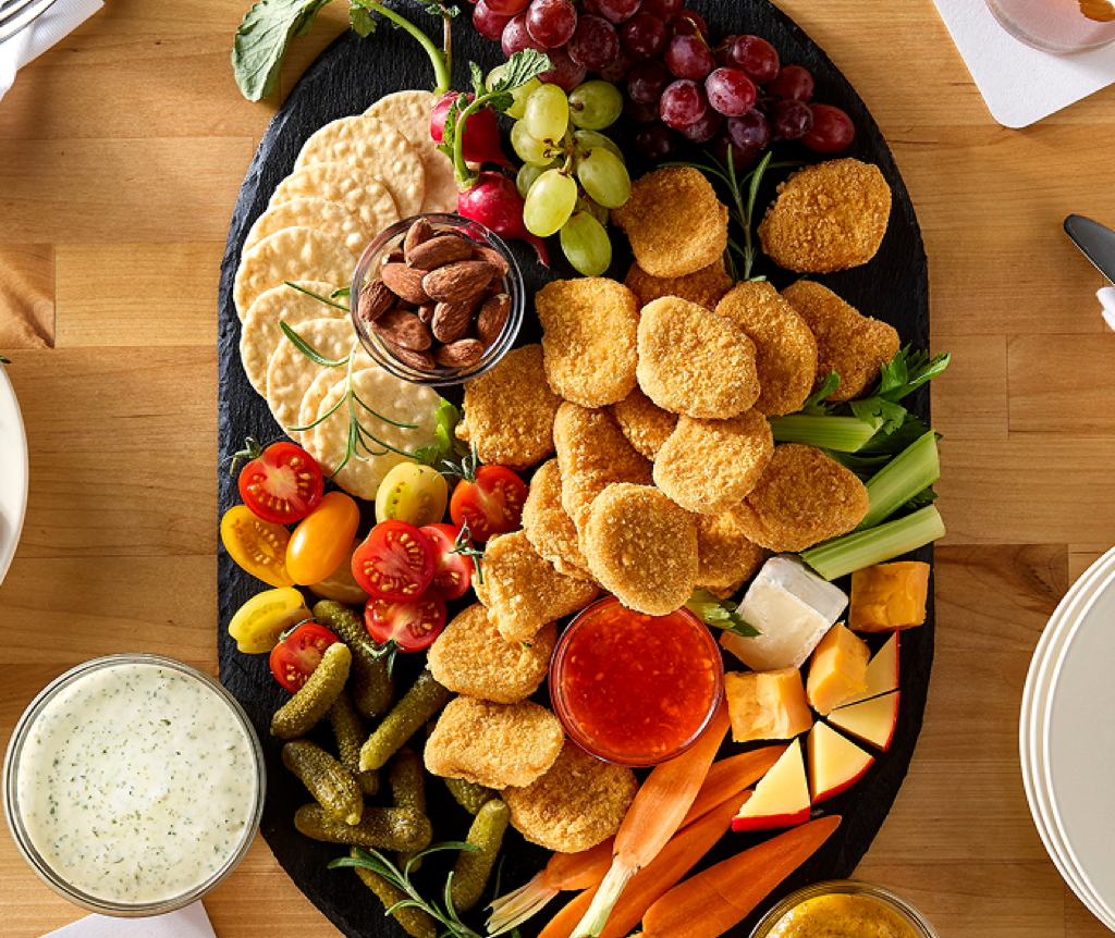 Gluten-free chicken nuggets on a board with vegetables, fruit, crackers, and sauces