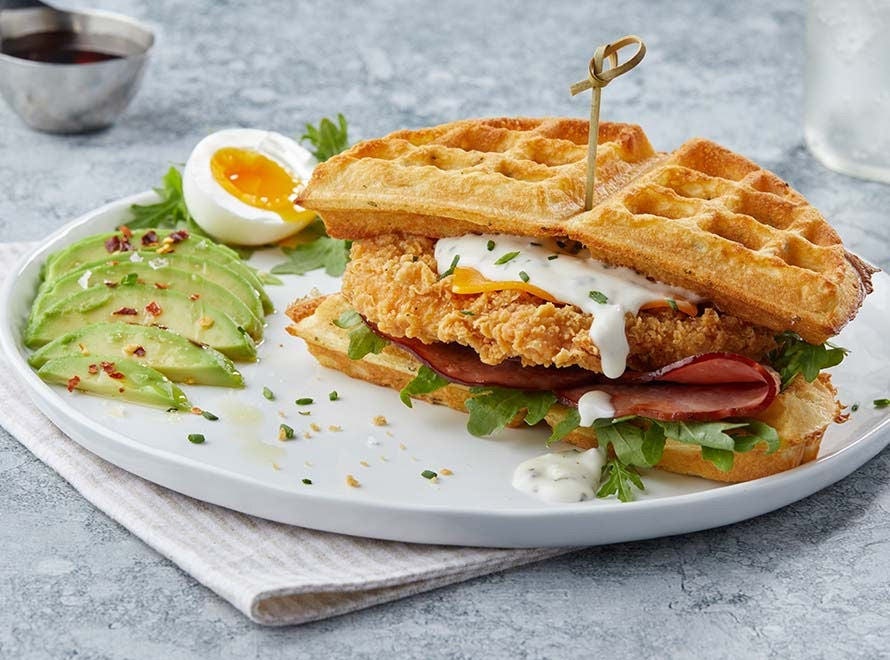 A plate with a breaded chicken breast filet sandwiched between two waffles with cheese