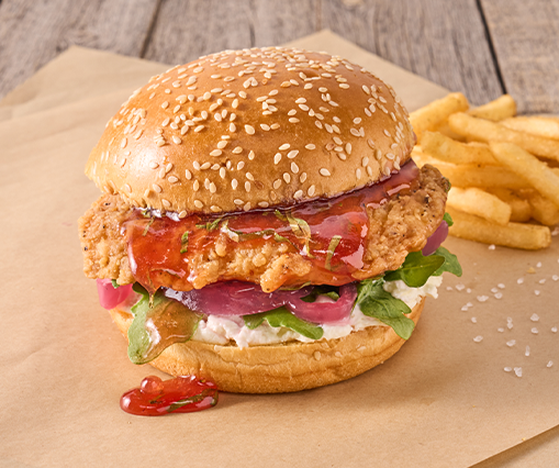 fried chicken sandwich with strawberry sauce on a sesame seed bun sits on top of a sheet of brown paper
