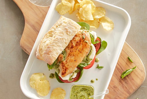 Sandwich with roasted chicken breast, tomato, mozzarella, basil pesto and greens on ciabatta, served with potato chips