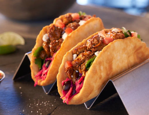Mexican fry-bread tacos with chicken, cabbage, tomatoes, and cotija on a slate platter in a kitchen setting
