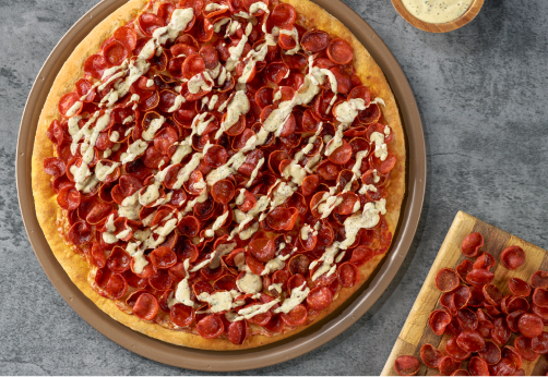 Pepperoni pizza with sauce drizzled on top with a plate of cupping pepperoni off to the side.