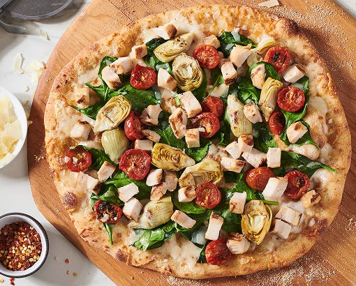 pizza is topped with diced chicken, fresh tomatoes, artichoke hearts, mozzarella cheese and white sauce